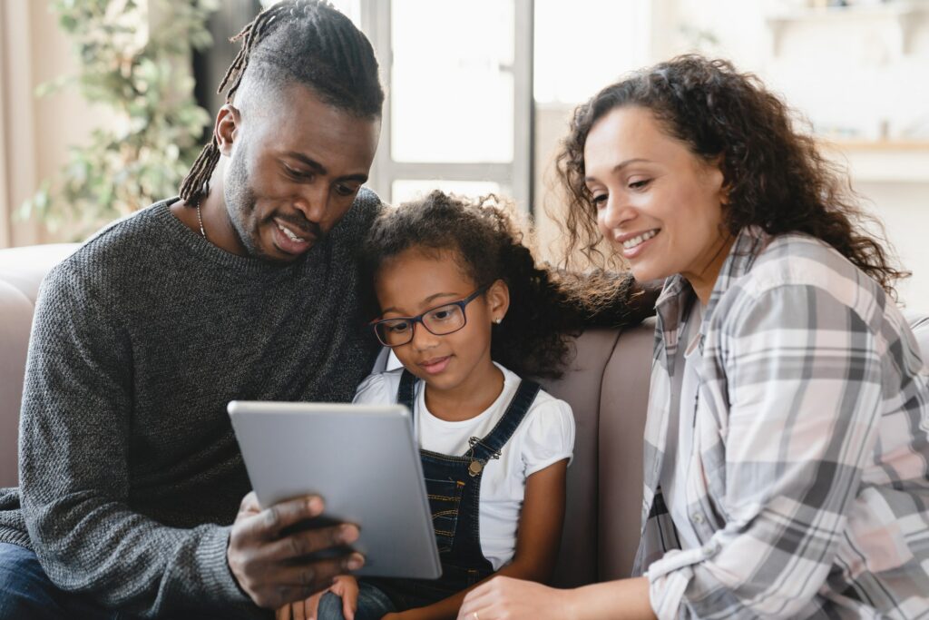 Parents with daughter using tablet relaxing at home, browsing mobile applications online