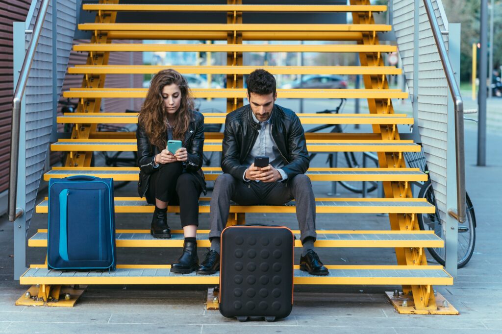 Couple with luggage, using mobile phone on steps, Florence, Italy
