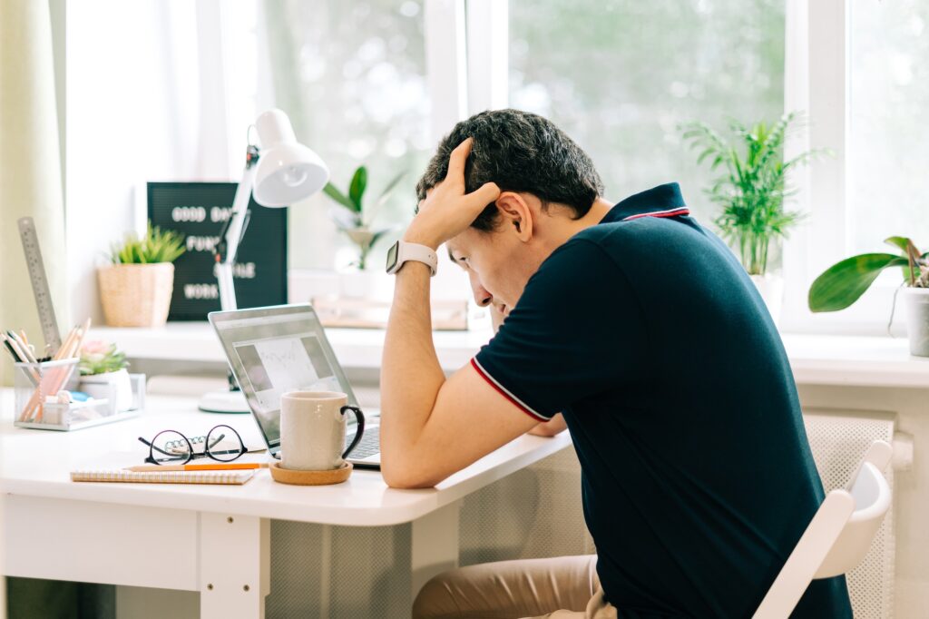 Man holding head, working from home at laptop.